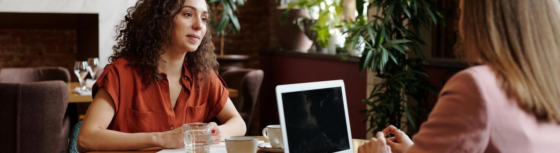 two women talking together while working on a computer