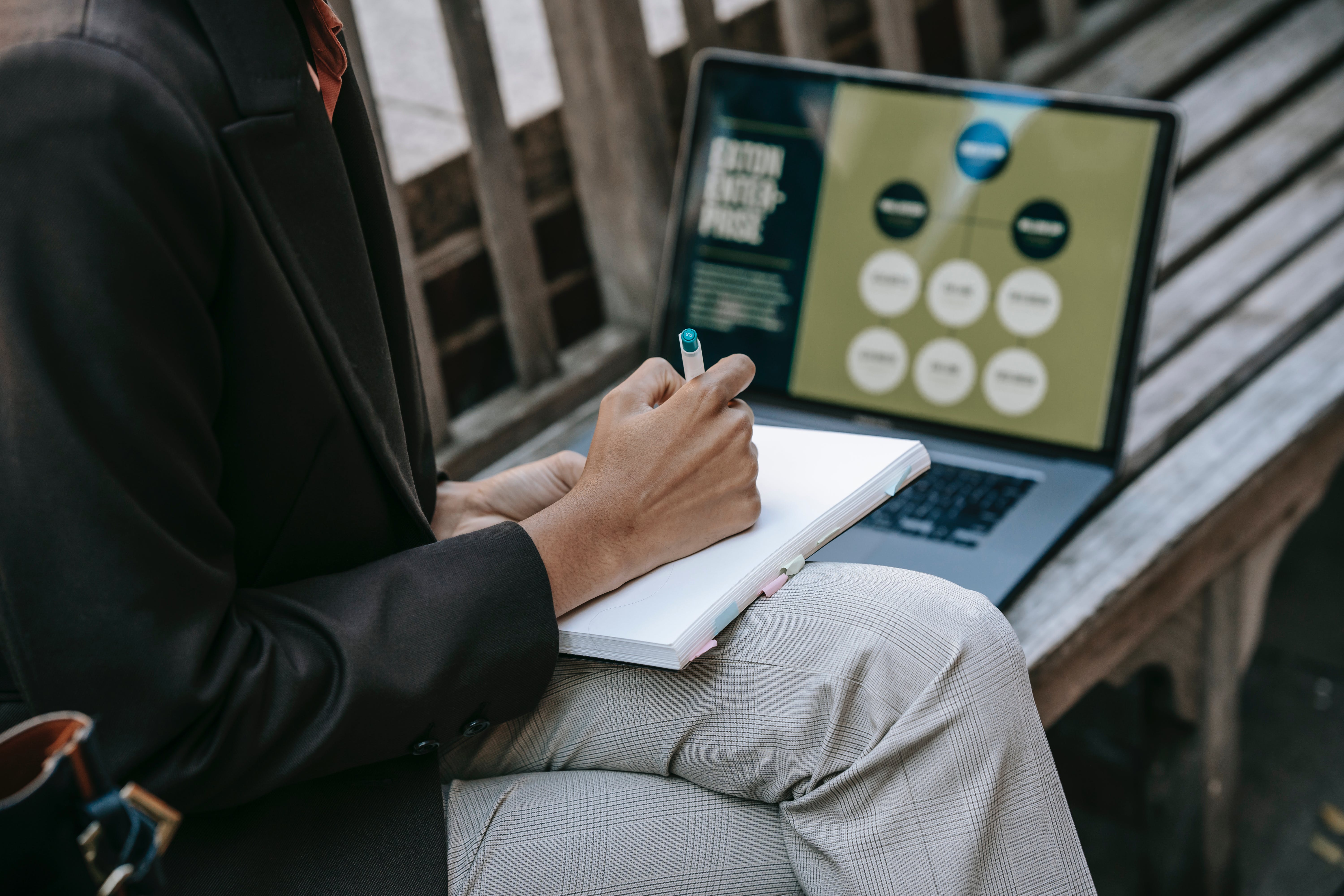 image of a person taking notes while viewing a presentation on a laptop